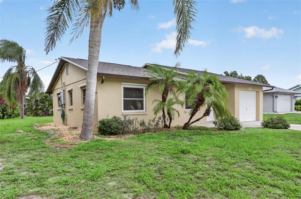 A tan, single-story house with a garage and palm trees on a grassy lawn — 10136 PEACH AVENUE, ENGLEWOOD, FL