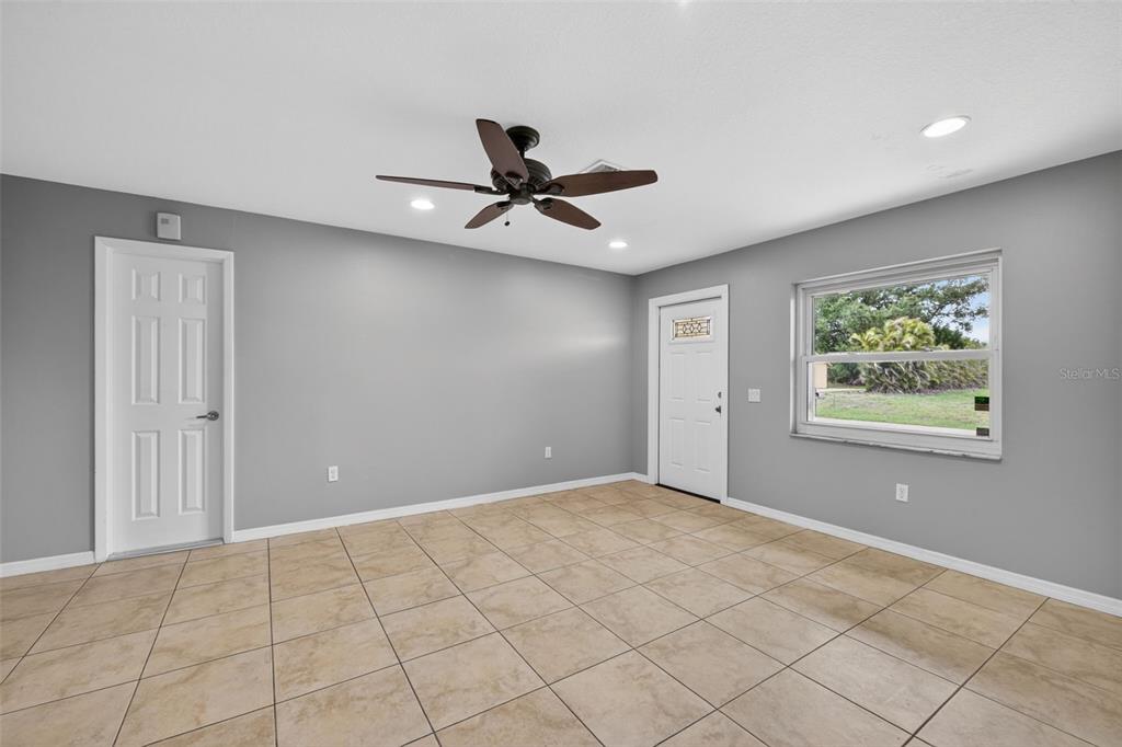 An empty room with gray walls, beige tile flooring, a ceiling fan, and two doors — 10136 PEACH AVENUE, ENGLEWOOD, FL