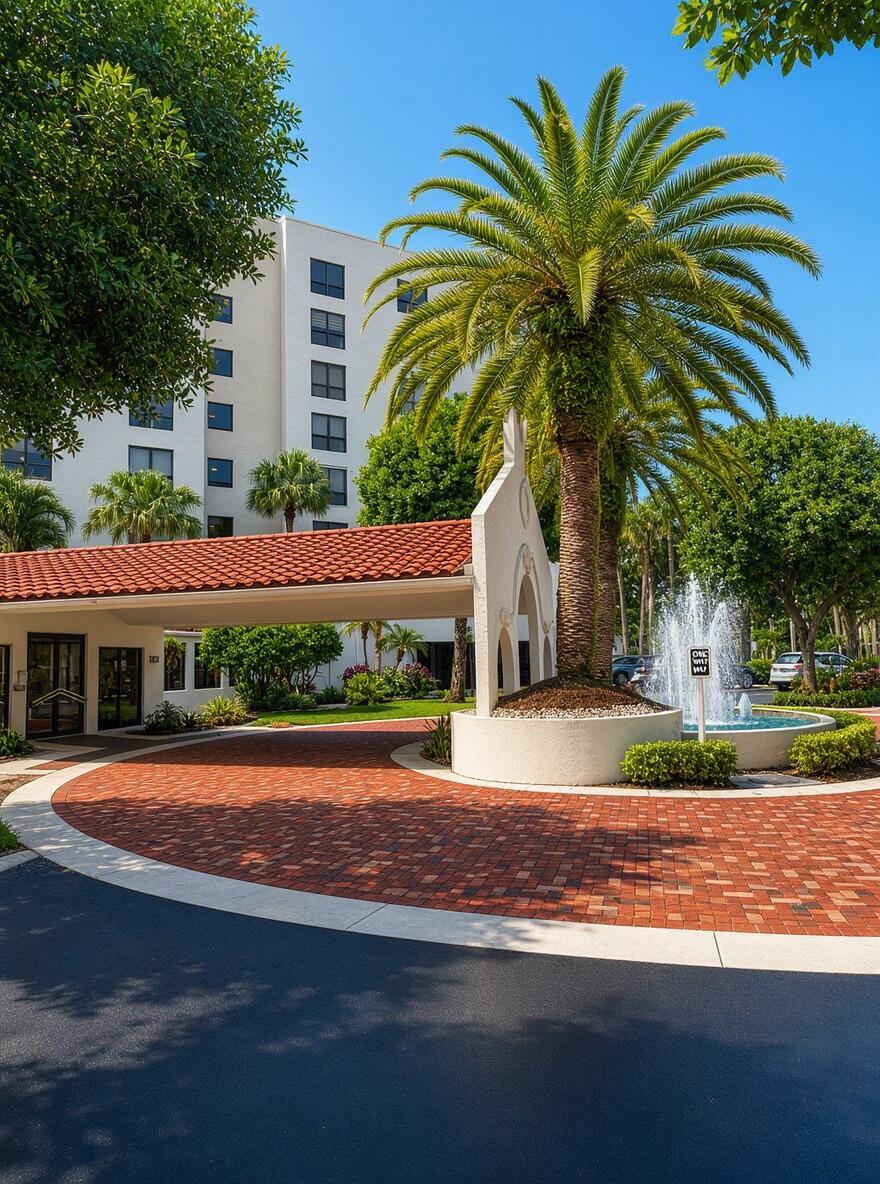 A palm tree and fountain stand in front of a building with a red-tiled porte-cochère — 7567 Imperial Drive # 202, Boca Raton FL 33433, BOCA RATON, FL