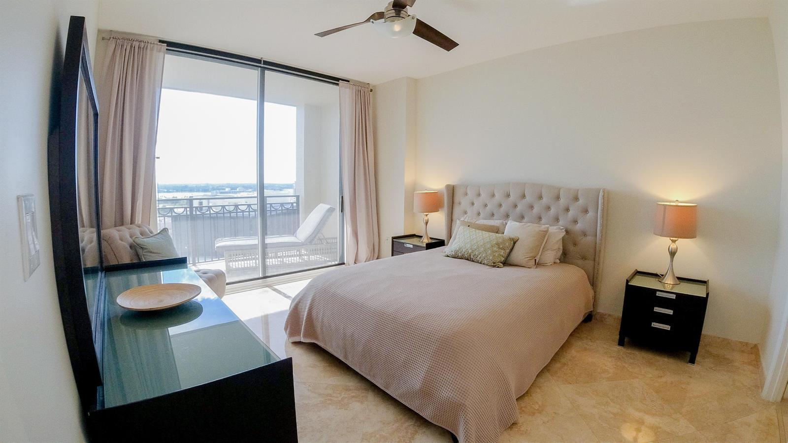 A bedroom features a tufted headboard, two nightstands, and a sliding door leading to a balcony — 550 Okeechobee Boulevard # 1721, West Palm Beach FL 33401, WEST PALM BEACH, FL