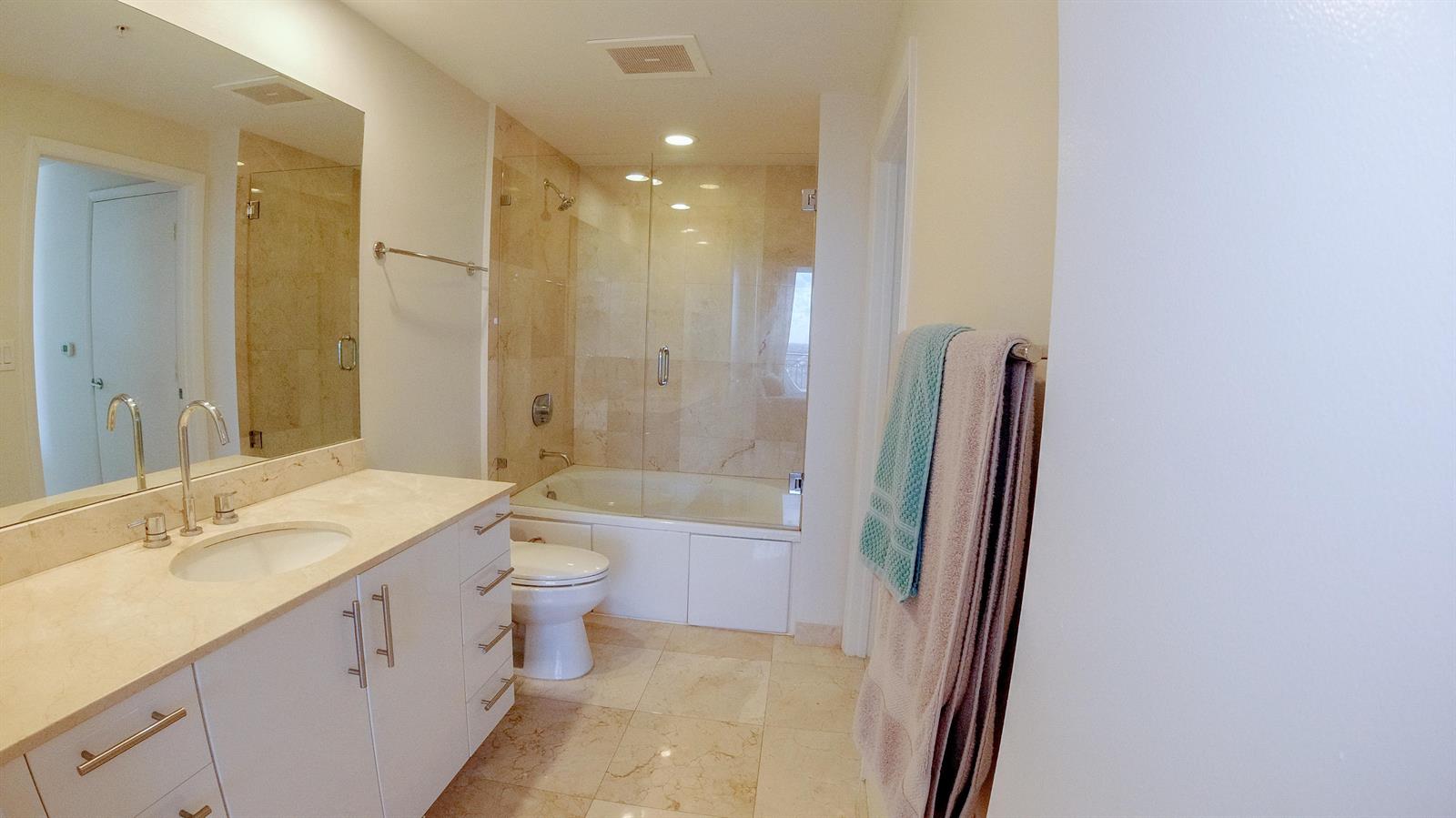 A bathroom features a white vanity, marble countertops, a toilet, and a glass-enclosed tub shower — 550 Okeechobee Boulevard # 1721, West Palm Beach FL 33401, WEST PALM BEACH, FL