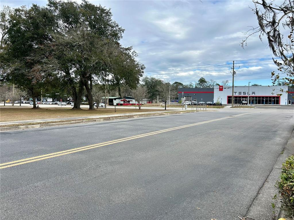 A Tesla dealership building stands across a paved road near a large tree — 2550 N MAIN STREET, GAINESVILLE, FL
