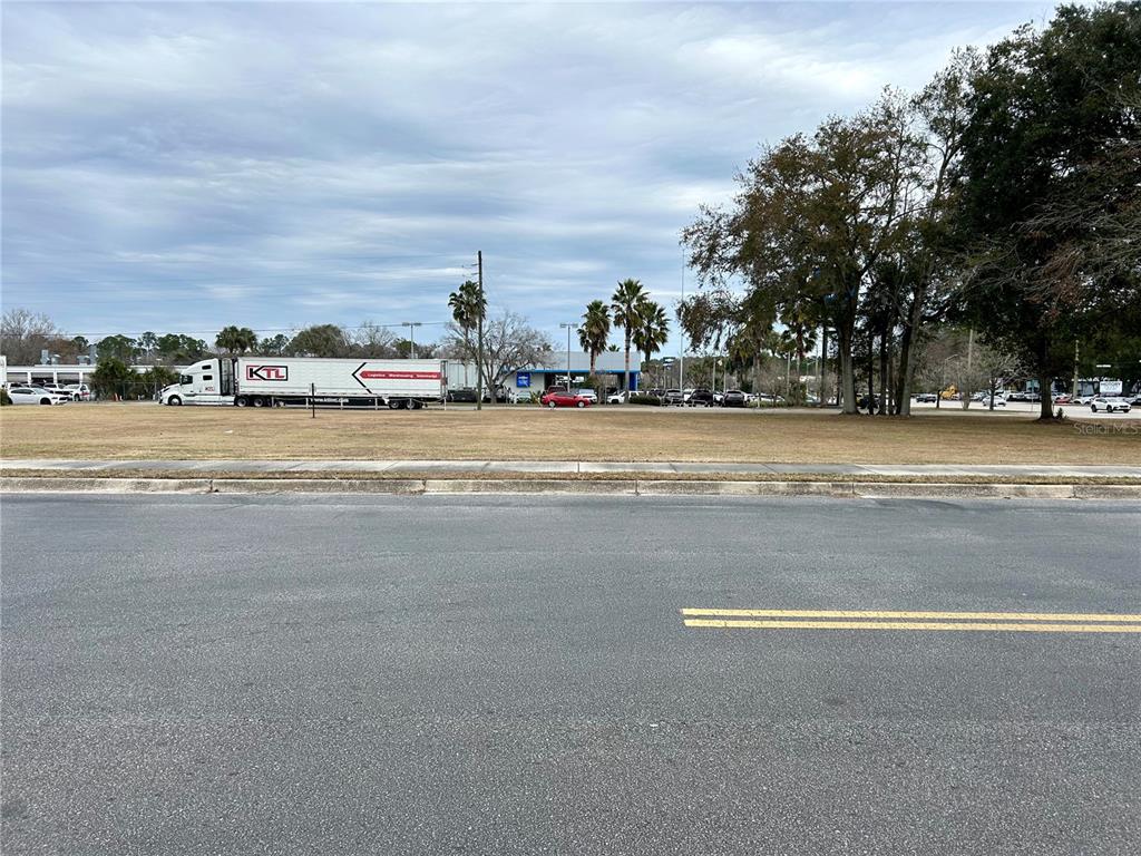 A vacant, grassy lot sits adjacent to a paved road with a semi-truck parked nearby — 2550 N MAIN STREET, GAINESVILLE, FL