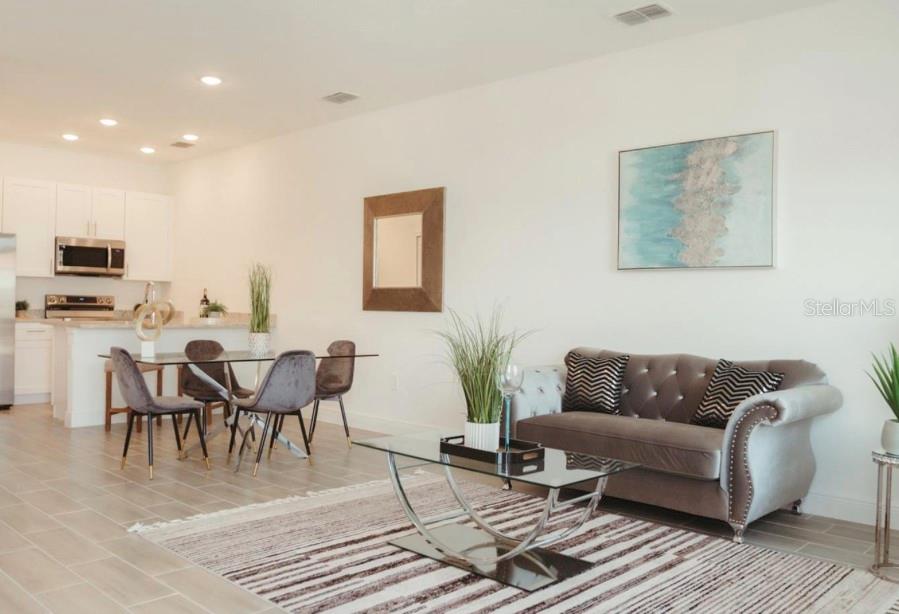 An open-concept living and dining area features a grey tufted sofa and glass-topped tables — 1740 PACIFIC ROAD, KISSIMMEE, FL