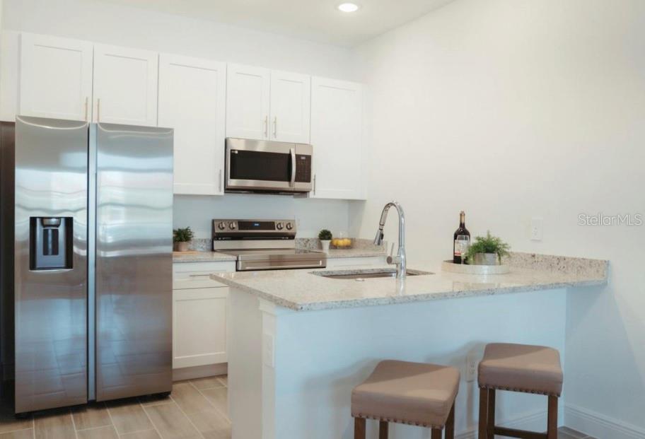 A kitchen features white cabinets, stainless steel appliances, and a granite-topped island with bar stools — 1740 PACIFIC ROAD, KISSIMMEE, FL