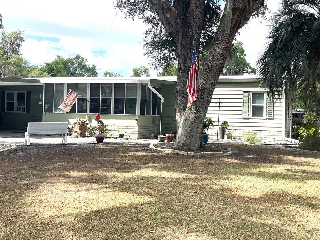 A single-story house with light green siding features a large tree and American flag — 2 S. BOBWHITE RD, WILDWOOD, FL