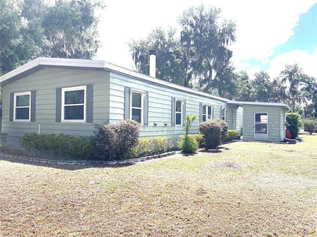 A light green single-story manufactured home with a metal roof and surrounding trees — 2 S. BOBWHITE RD, WILDWOOD, FL