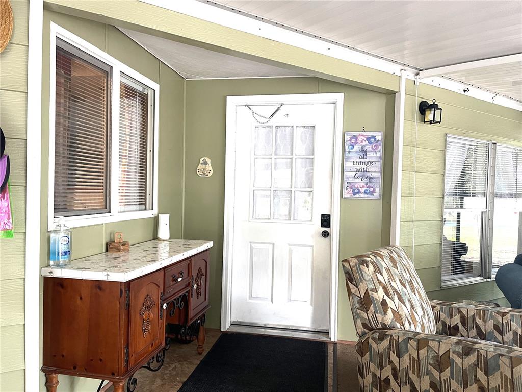 A covered porch features a white front door, a wooden sideboard, and a patterned armchair — 2 S. BOBWHITE RD, WILDWOOD, FL