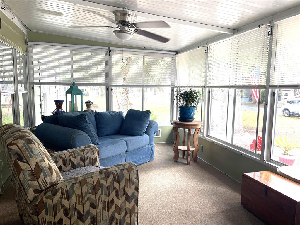 A sunroom features a blue sofa, patterned armchair, ceiling fan, and large windows with blinds — 2 S. BOBWHITE RD, WILDWOOD, FL