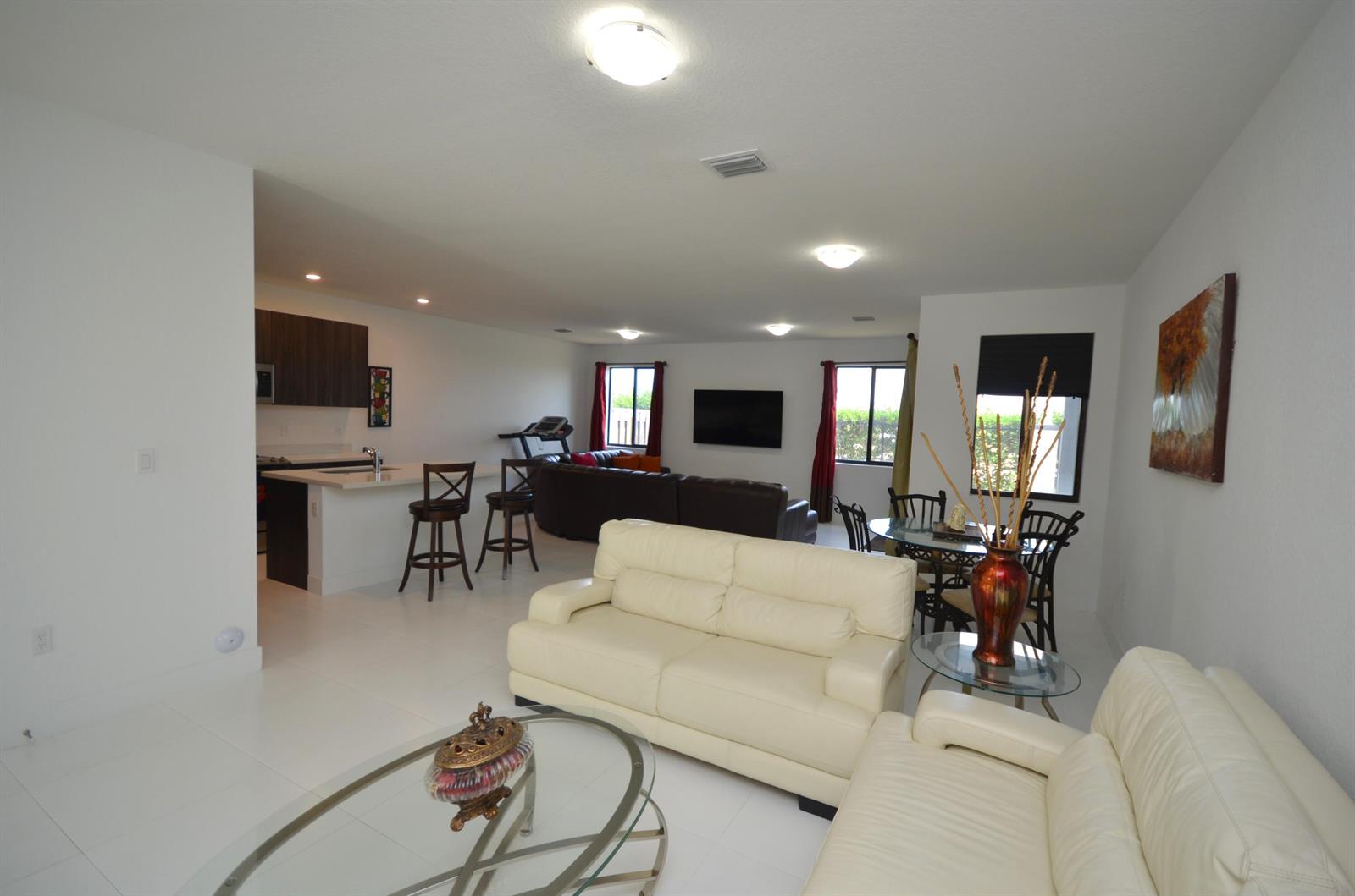 An open-concept living and dining area features white tile floors, cream leather sofas, and kitchen — 15743 SW 136th Terrace, Miami FL 33196, MIAMI, FL