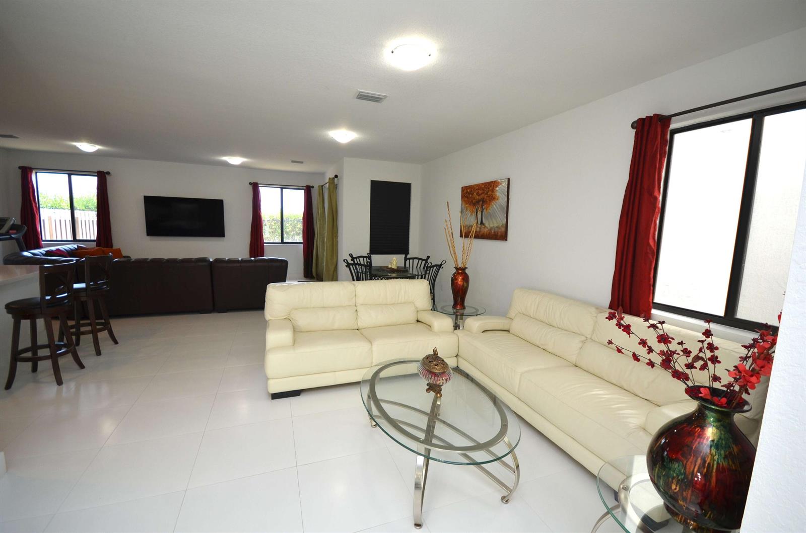 A spacious living room features white tile floors, two cream-colored sofas, and red curtains — 15743 SW 136th Terrace, Miami FL 33196, MIAMI, FL
