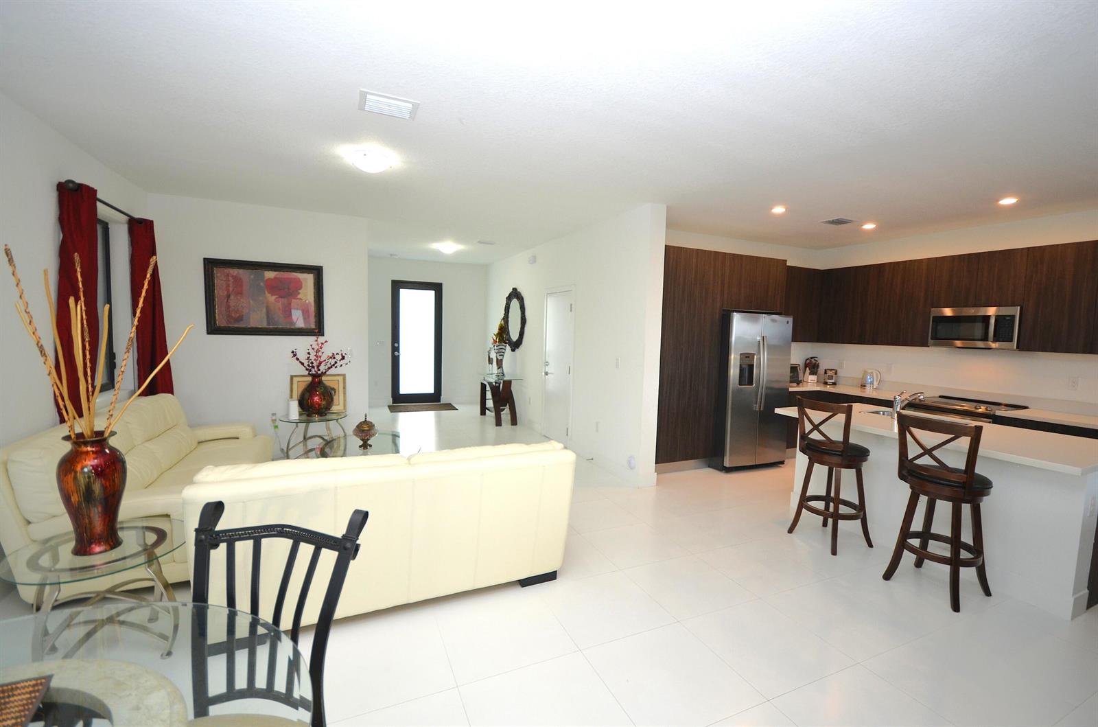 An open-concept living room and kitchen featuring white tile floors and dark wood cabinetry — 15743 SW 136th Terrace, Miami FL 33196, MIAMI, FL