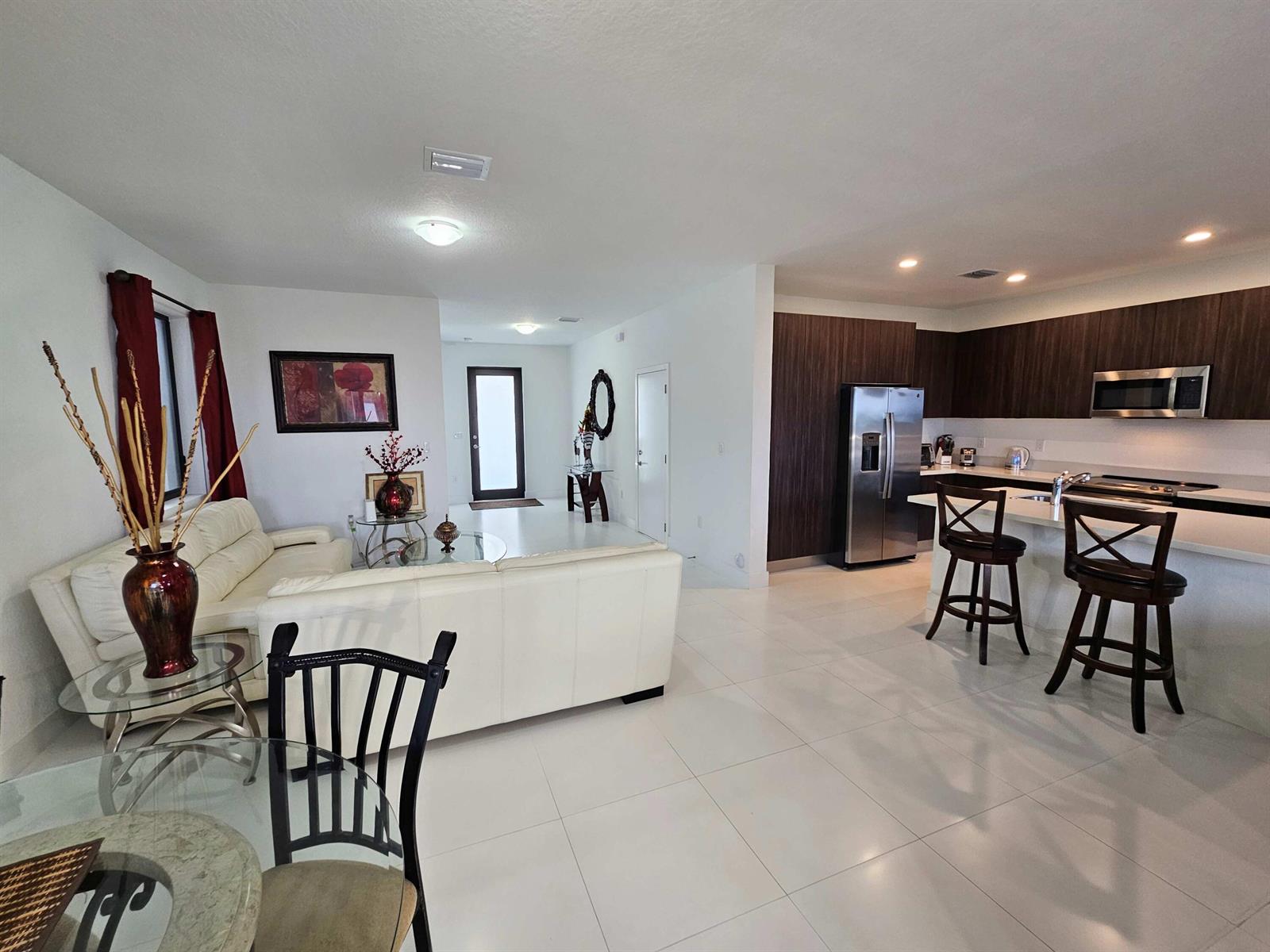 An open-concept living room and kitchen featuring white tile floors and dark wood cabinetry — 15743 SW 136th Terrace, Miami FL 33196, MIAMI, FL