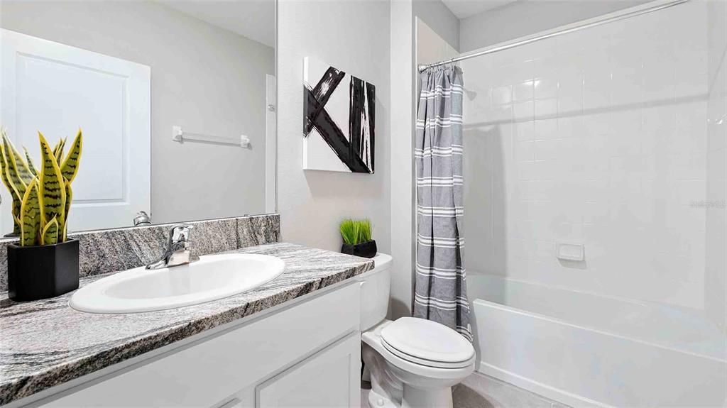 A bathroom features a granite vanity, white cabinets, a toilet, and a shower-tub combination — 10824 QUAIL GROVE WAY, SAN ANTONIO, FL