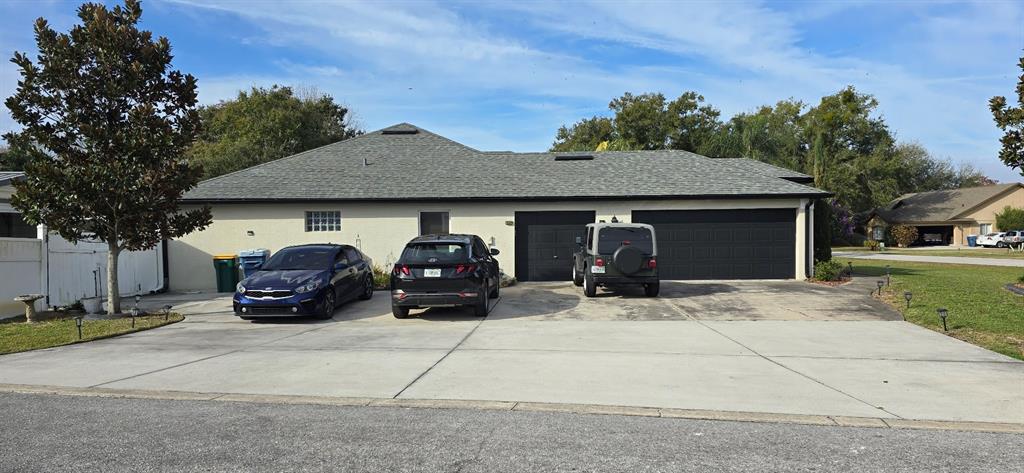 A single-story house with a large concrete driveway, three parked vehicles, and two garage doors — 336 LAKECREST DRIVE, TAVARES, FL