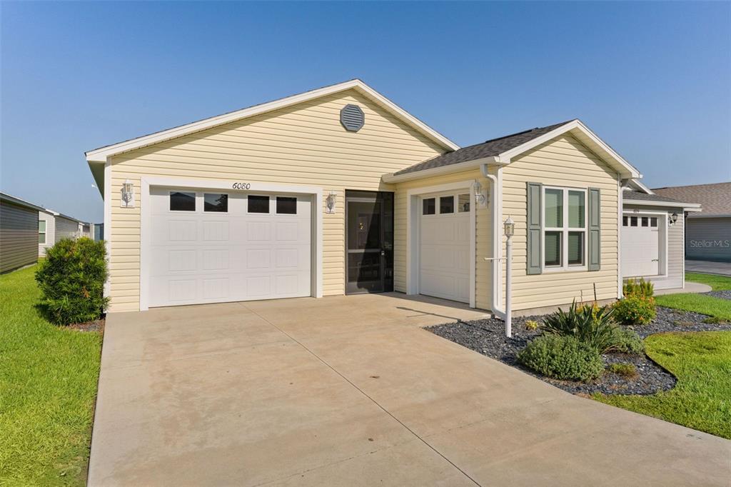 A yellow, single-story suburban house features a two-car garage, a concrete driveway, and shutters — 6080 ALLEN AVENUE, THE VILLAGES, FL