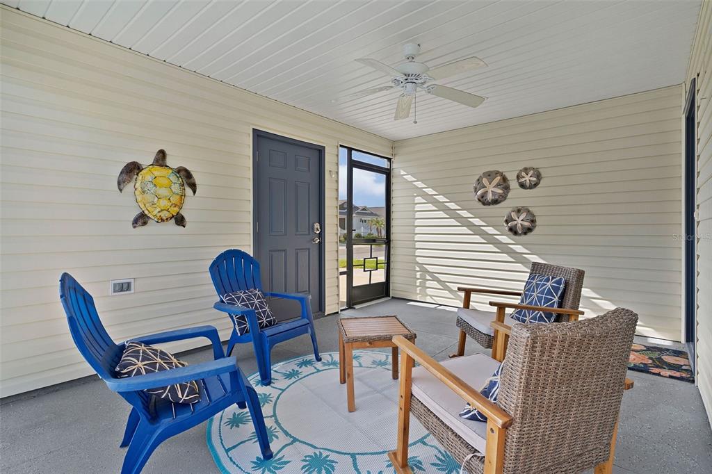 A covered porch features blue and wicker chairs, a small table, and coastal wall decor — 6080 ALLEN AVENUE, THE VILLAGES, FL