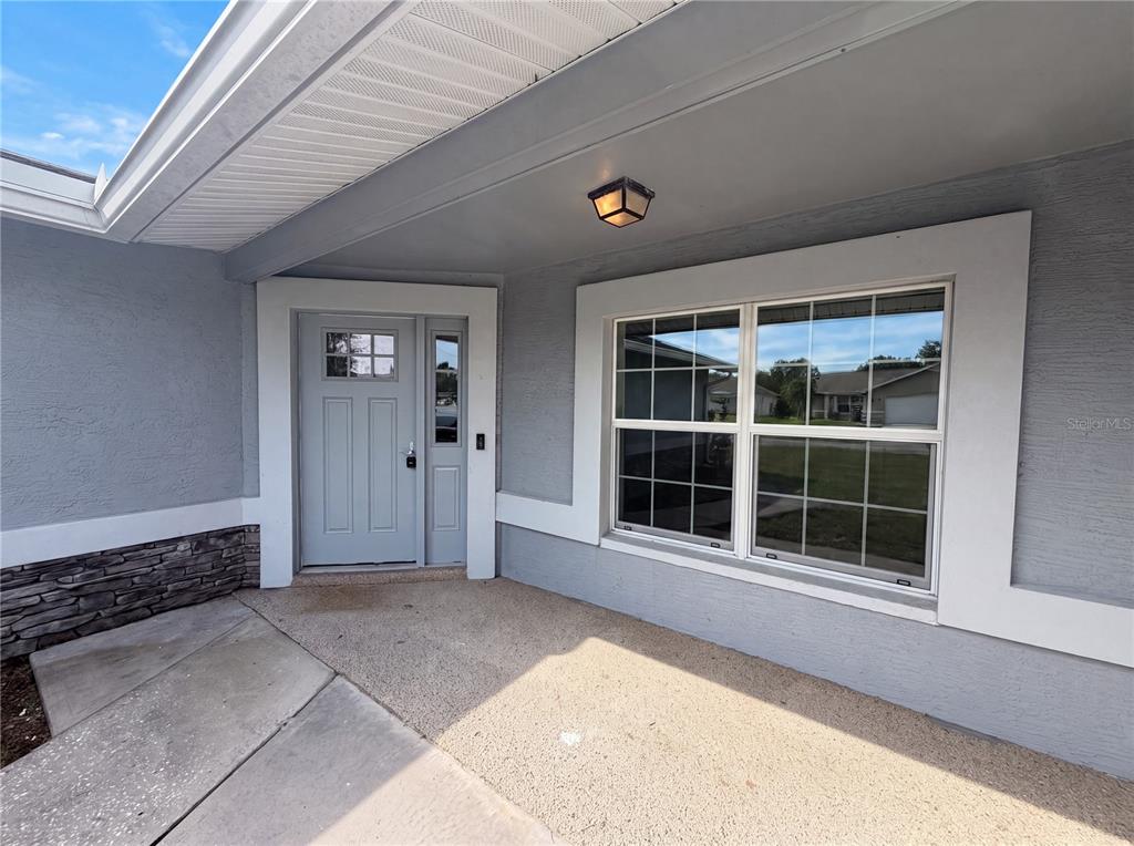 A gray-painted house exterior features a front door, a large window, and stone accents — 3333 AGAR AVENUE, SPRING HILL, FL