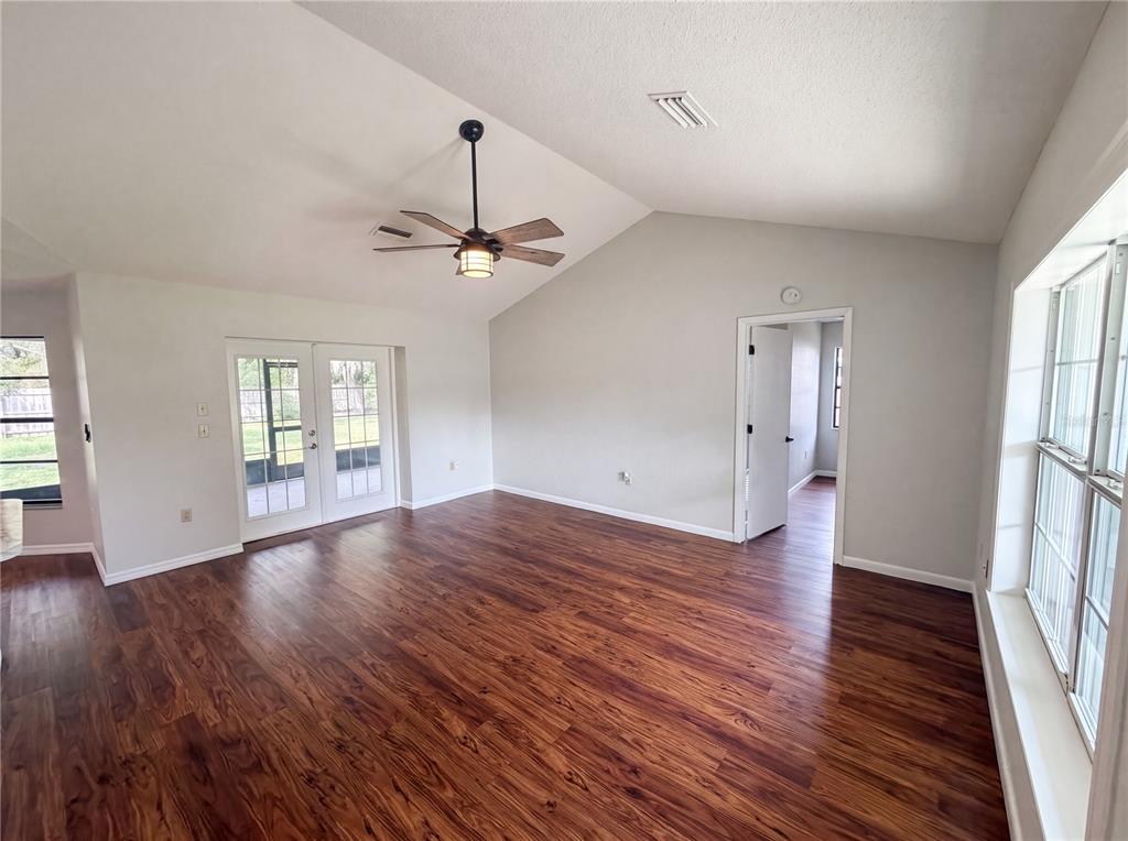 An empty living room features wood-look flooring, a vaulted ceiling with a fan, and glass doors — 3333 AGAR AVENUE, SPRING HILL, FL