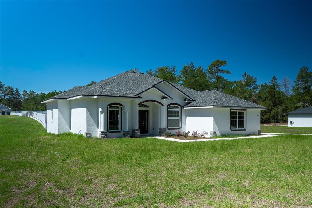A white stucco single-story house with a gray shingled roof sits on a grassy lot — 17820 SW 33RD TERRACE, OCALA, FL