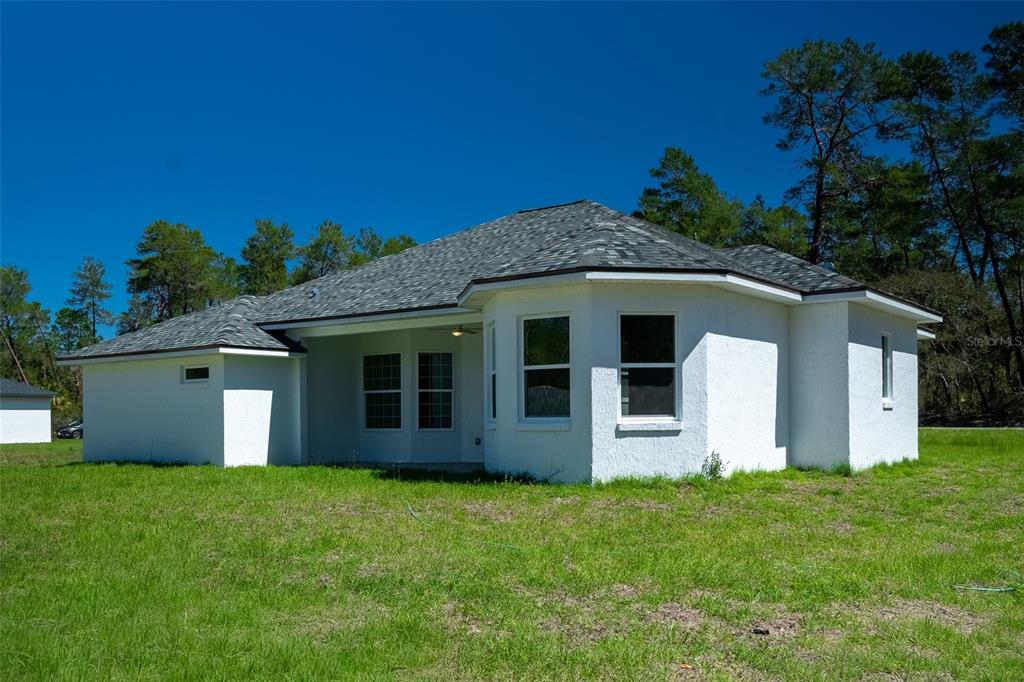 The exterior rear view of a white stucco house with a gray shingled roof — 17820 SW 33RD TERRACE, OCALA, FL