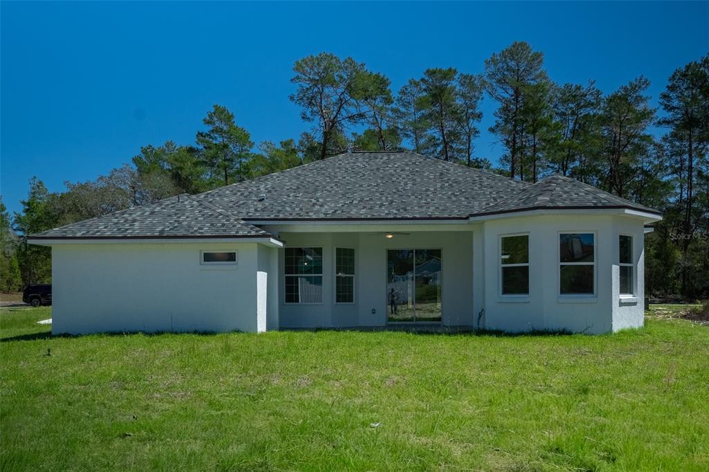 The rear exterior of a white single-story house with a covered patio and grassy yard — 17820 SW 33RD TERRACE, OCALA, FL