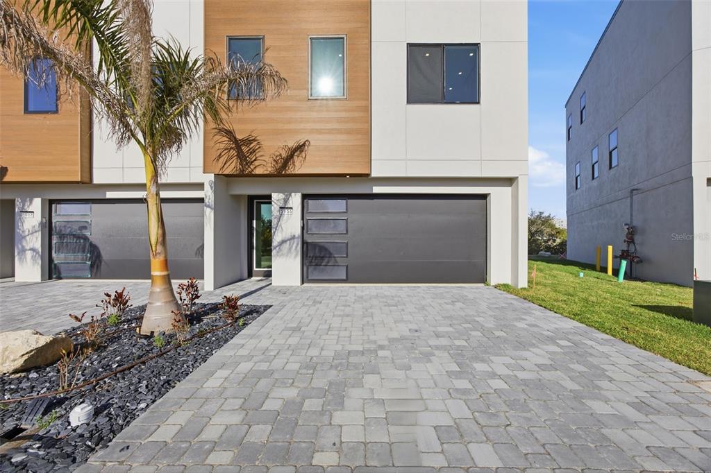 A modern townhouse exterior features a paved driveway, a two-car garage, and wood-paneled accents — 5956 AQUA RESERVE BOULEVARD, NEW PORT RICHEY, FL