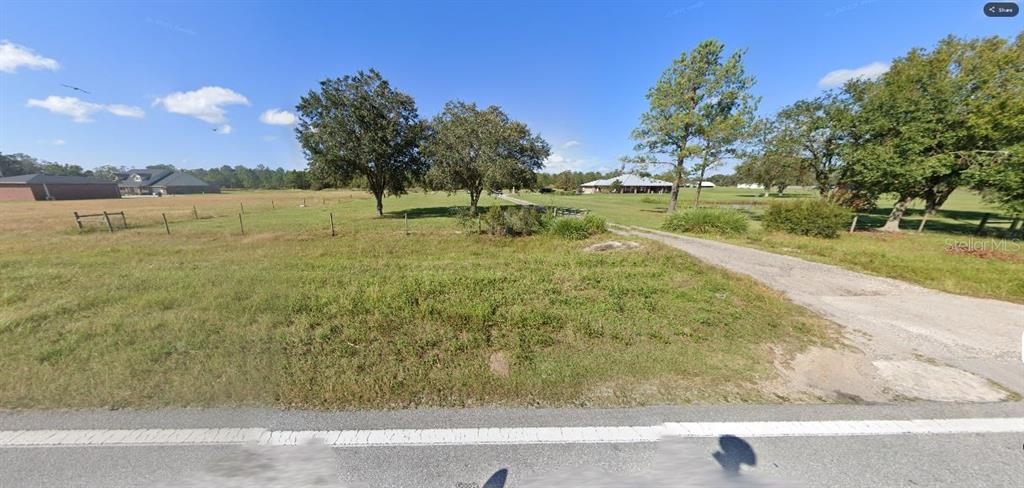 A grassy, open lot with a gravel driveway, scattered trees, and a distant house — OLD GRADE RD, POLK CITY, FL