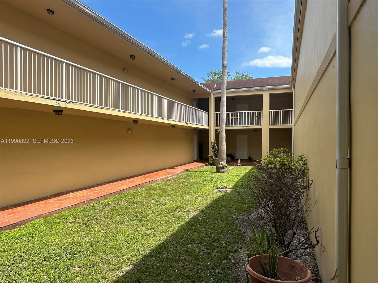 An exterior view shows a grassy courtyard between two levels of apartment building balconies — 13810 SW 112th St # 106, Miami FL 33186, MIAMI, FL