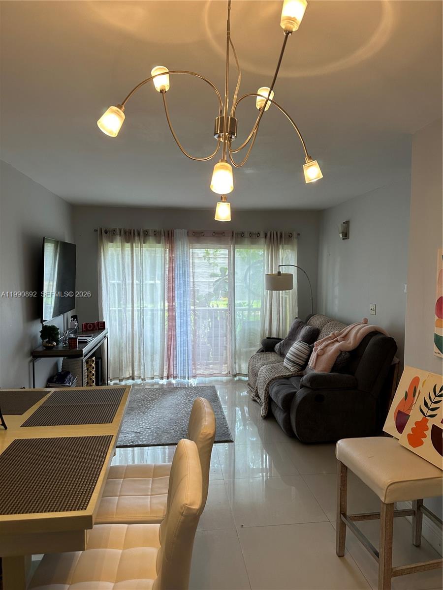 A living and dining area features tile floors, a modern chandelier, and a sliding glass door — 13810 SW 112th St # 106, Miami FL 33186, MIAMI, FL