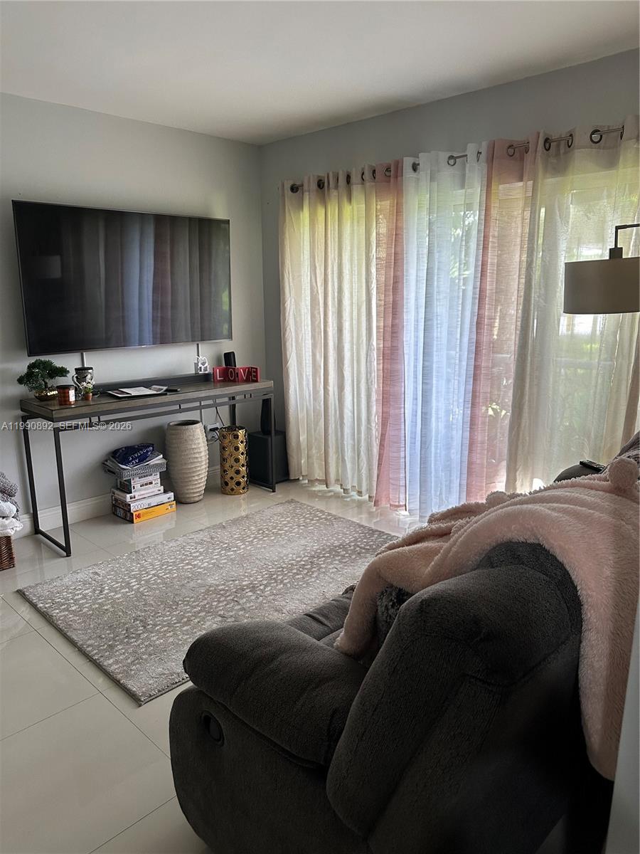 A living room features a wall-mounted television, a console table, a rug, and sheer curtains — 13810 SW 112th St # 106, Miami FL 33186, MIAMI, FL
