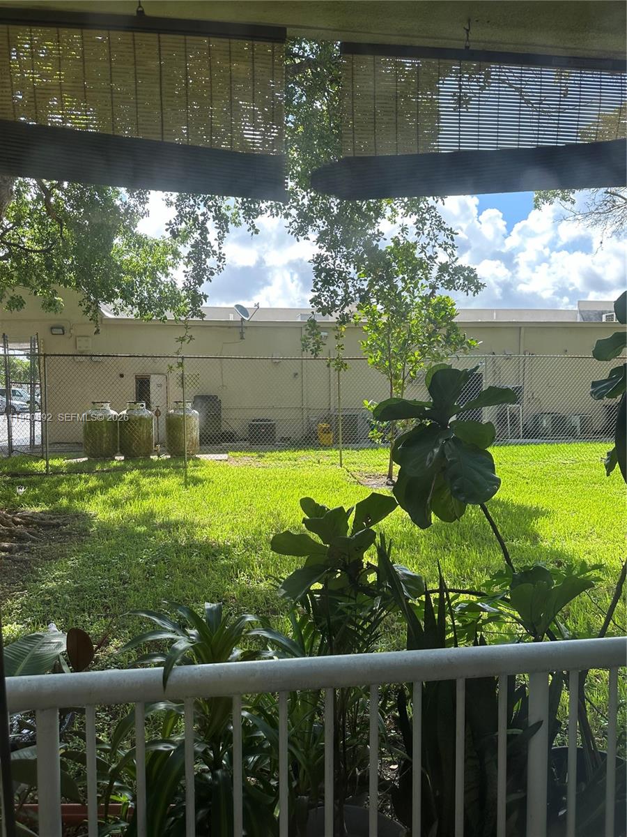 A view from a balcony overlooking a grassy yard with propane tanks and a fence — 13810 SW 112th St # 106, Miami FL 33186, MIAMI, FL