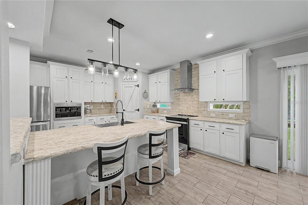 A kitchen features white cabinets, a stone backsplash, a kitchen island, and stainless steel appliances — 11293 CLEEVER STREET, WEEKI WACHEE, FL