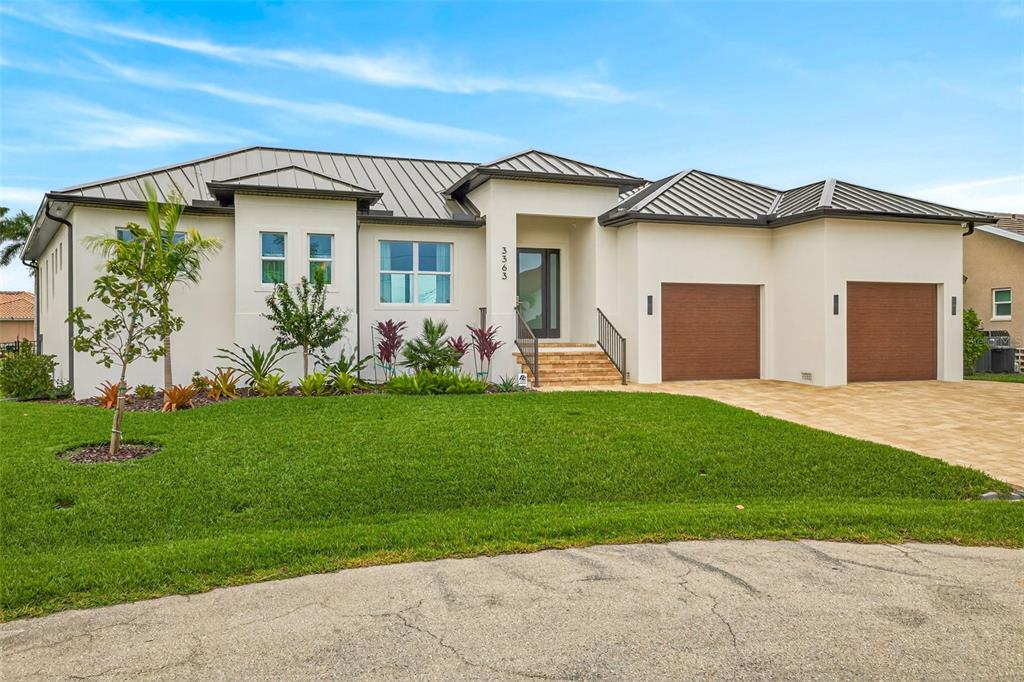 A modern single-story house with a metal roof, two garage doors, and landscaped front yard — 3363 TRINIDAD COURT, PUNTA GORDA, FL