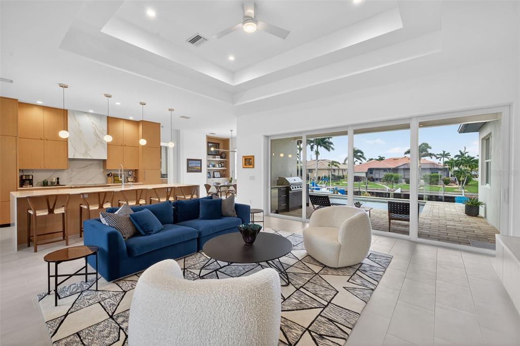 A modern living room with a blue sofa, white chairs, and sliding doors to a patio — 3363 TRINIDAD COURT, PUNTA GORDA, FL