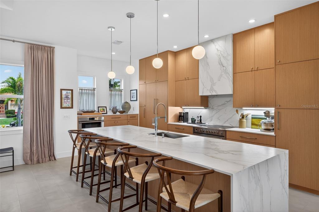 A modern kitchen features light wood cabinetry, a marble waterfall island, and four wooden chairs — 3363 TRINIDAD COURT, PUNTA GORDA, FL