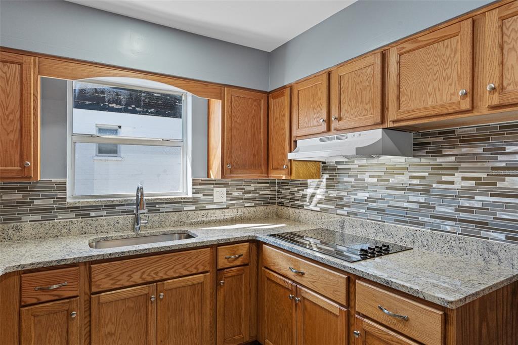 A kitchen with oak cabinets, granite countertops, a tiled backsplash, and a stainless steel sink — 417 MANHATTAN AVENUE, DAYTONA BEACH, FL