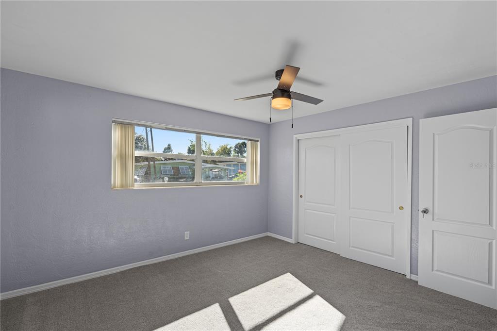 A bedroom features light purple walls, gray carpeting, a ceiling fan, and white closet doors — 417 MANHATTAN AVENUE, DAYTONA BEACH, FL