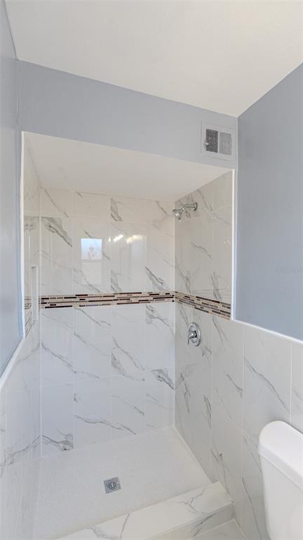 A walk-in shower with white marble-look tile walls and a horizontal decorative accent strip — 417 MANHATTAN AVENUE, DAYTONA BEACH, FL