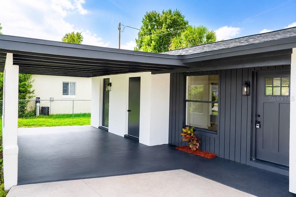 A modern home exterior features a dark gray carport, matching front door, and white walls — 4443 KING COLE BOULEVARD, ORLANDO, FL