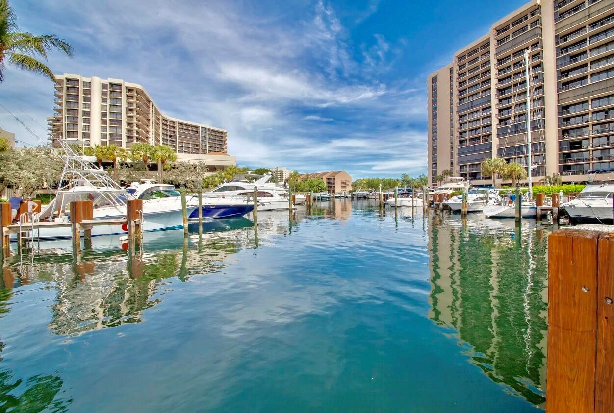 A marina with several docked yachts sits between two large residential buildings under a blue sky — 4748 S Ocean Boulevard # a, Highland Beach FL 33487, HIGHLAND BEACH, FL