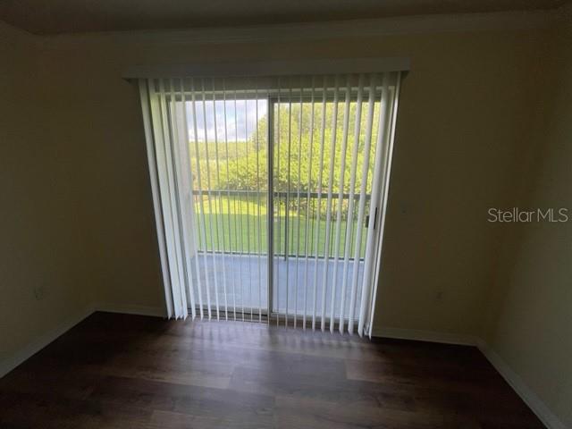 An empty room with wood-look flooring and vertical blinds covering a sliding glass door — 18108 PERREGRINES PERCH PLACE UNIT 211, LUTZ, FL