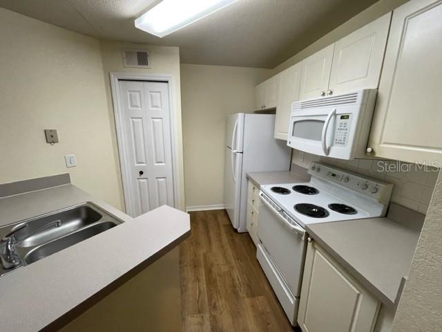 A kitchen features white cabinets, a white refrigerator, a white stove, and a double sink — 18108 PERREGRINES PERCH PLACE UNIT 211, LUTZ, FL