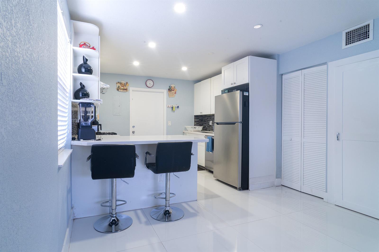 A kitchen features white cabinets, stainless steel appliances, a breakfast bar with stools, and tile flooring — 506 Worthmore Drive, FL 33460, FL