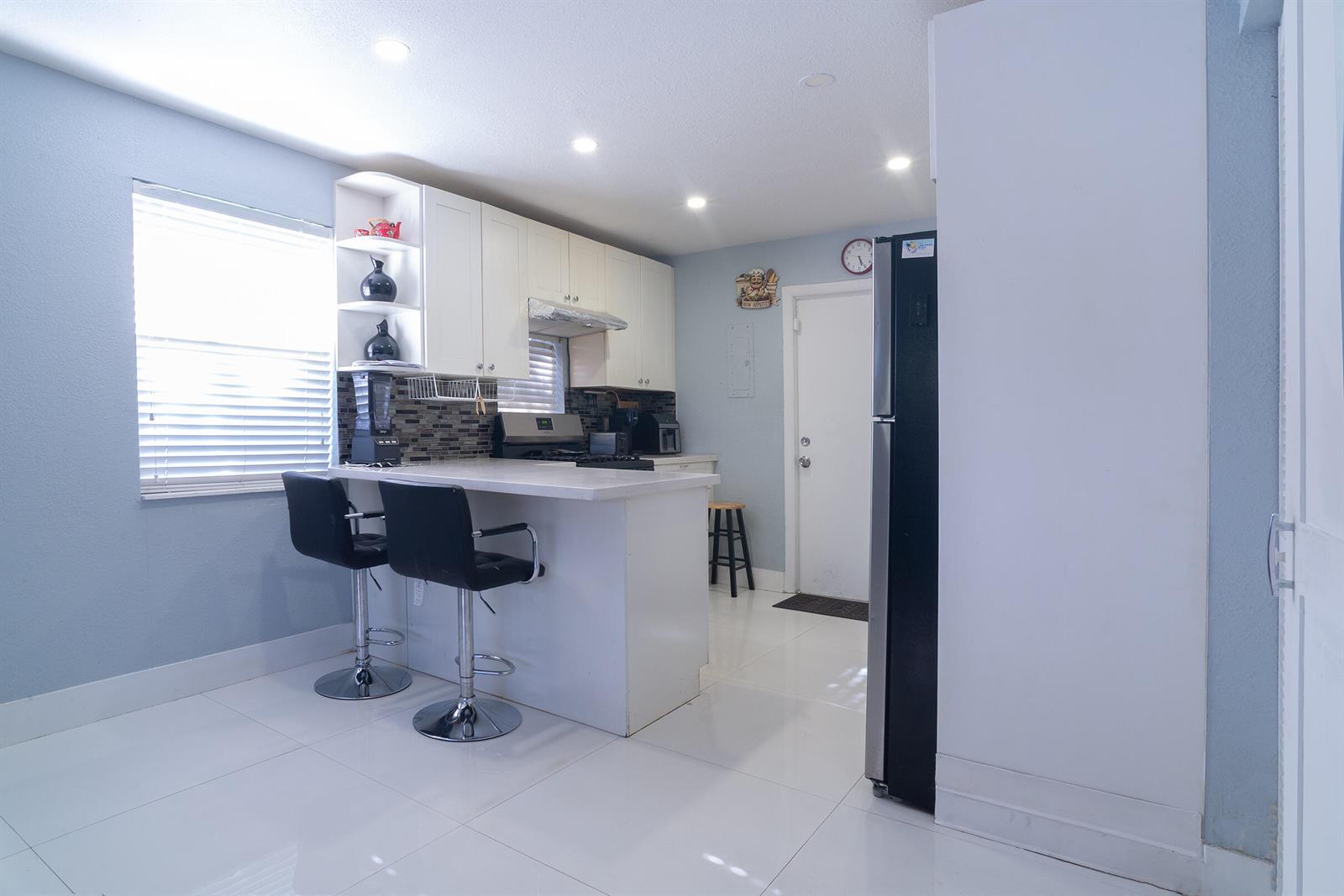 A kitchen features white cabinets, a breakfast bar with two stools, and light-colored tile flooring — 506 Worthmore Drive, FL 33460, FL