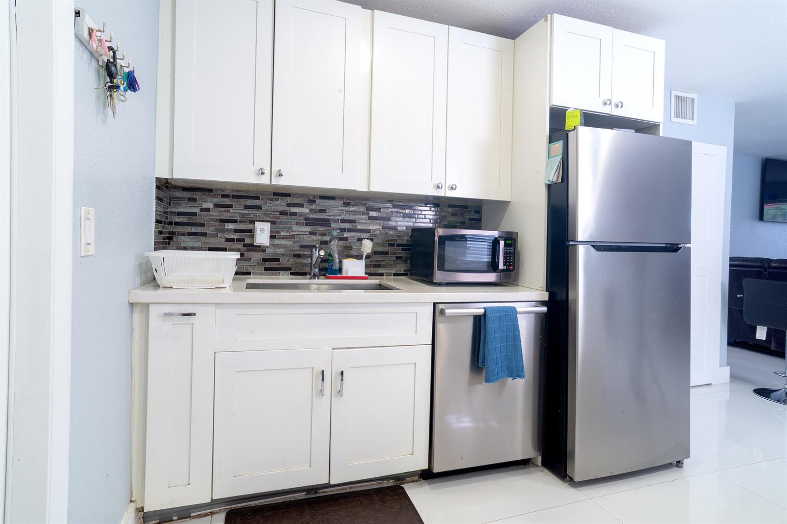A kitchen features white cabinets, stainless steel appliances, and a dark mosaic tile backsplash — 506 Worthmore Drive, FL 33460, FL
