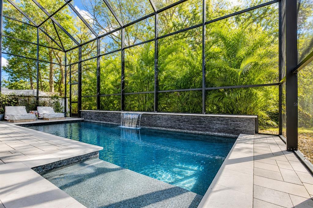 A screened-in swimming pool features a stone water feature wall and light-colored paver decking — 11403 QUIET FOREST DRIVE, TAMPA, FL