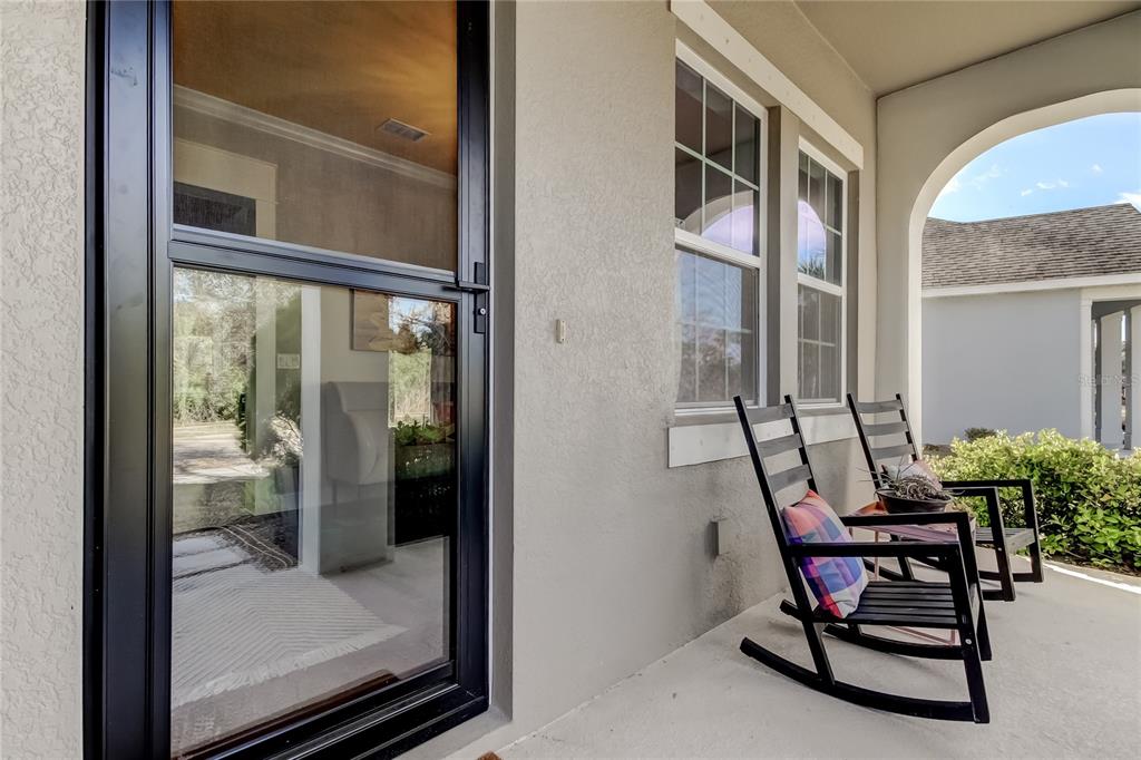 A covered porch features a glass storm door, two black rocking chairs, and beige stucco walls — 11403 QUIET FOREST DRIVE, TAMPA, FL