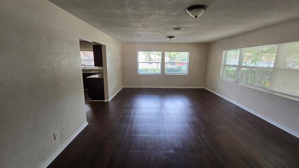 An empty living room features dark wood-look flooring, light-colored walls, and multiple windows — 14857 SUNSET STREET, CLEARWATER, FL