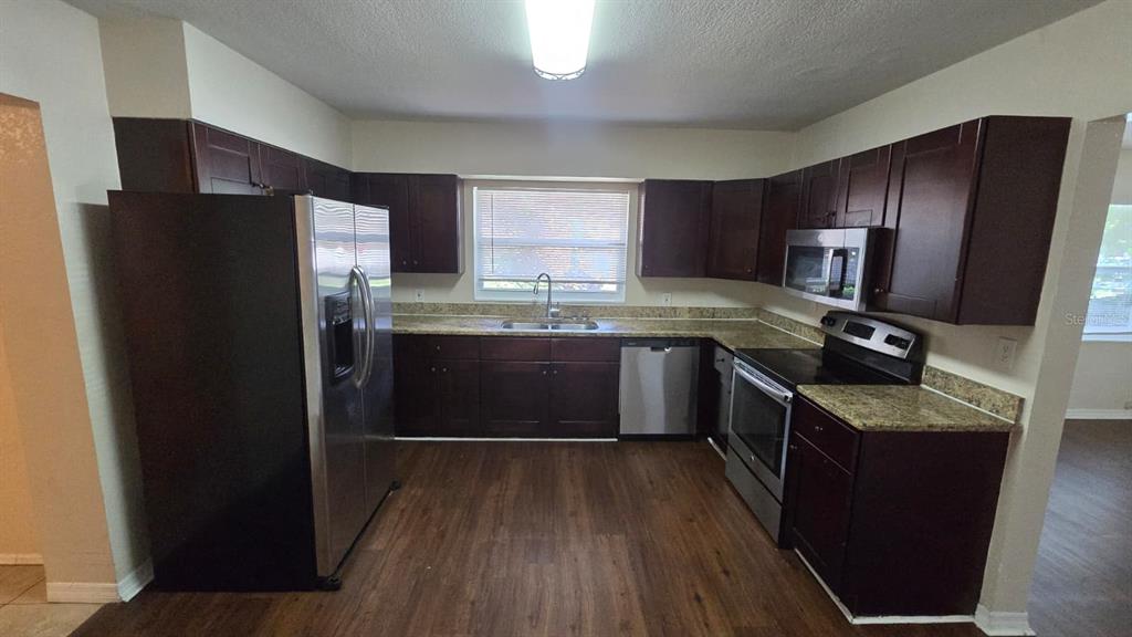 A kitchen features dark wood cabinets, stainless steel appliances, and granite countertops — 14857 SUNSET STREET, CLEARWATER, FL